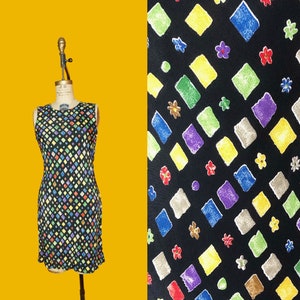 May include: A sleeveless black dress with a colourful geometric pattern of squares and diamonds. The dress has a fitted bodice and a straight skirt.