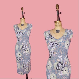 May include: A sleeveless dress with a V-neckline and a floral print in shades of blue, green, white, and pink. The dress has a fitted silhouette and a midi length.