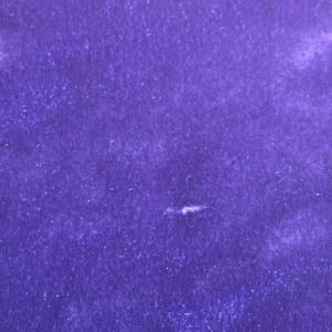 May include: A close-up of a piece of deep purple velvet fabric. The fabric has a soft, textured appearance with subtle variations in color and light. The rich, saturated hue of the velvet creates a luxurious feel.