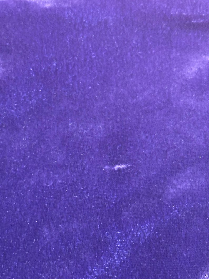 May include: A close-up of a piece of deep purple velvet fabric. The fabric has a soft, textured appearance with subtle variations in color and light. The rich, saturated hue of the velvet creates a luxurious feel.