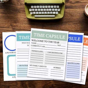 A table view with the 5 printable time capsule pages spread out on the table top. A typewriter, vase of flowers, plate of cookies and mug of coffee, some papers and a gift sit nearby.