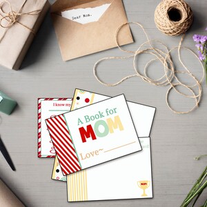May include: A collection of gift-giving supplies, including wrapped packages, a spool of twine, and a bouquet of purple flowers. Several greeting cards are visible, one reading "A Book for MOM". A pair of scissors and tape dispenser are also present.
