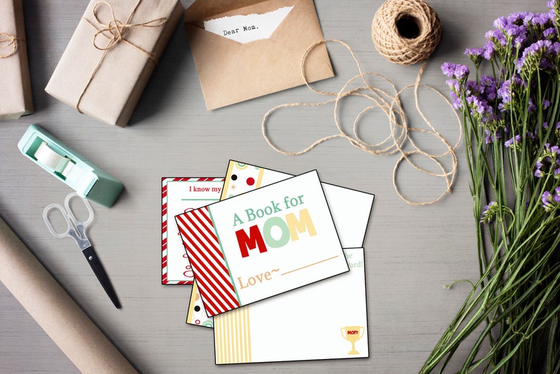 May include: A collection of gift-giving supplies, including wrapped packages, a spool of twine, and a bouquet of purple flowers. Several greeting cards are visible, one reading "A Book for MOM". A pair of scissors and tape dispenser are also present.