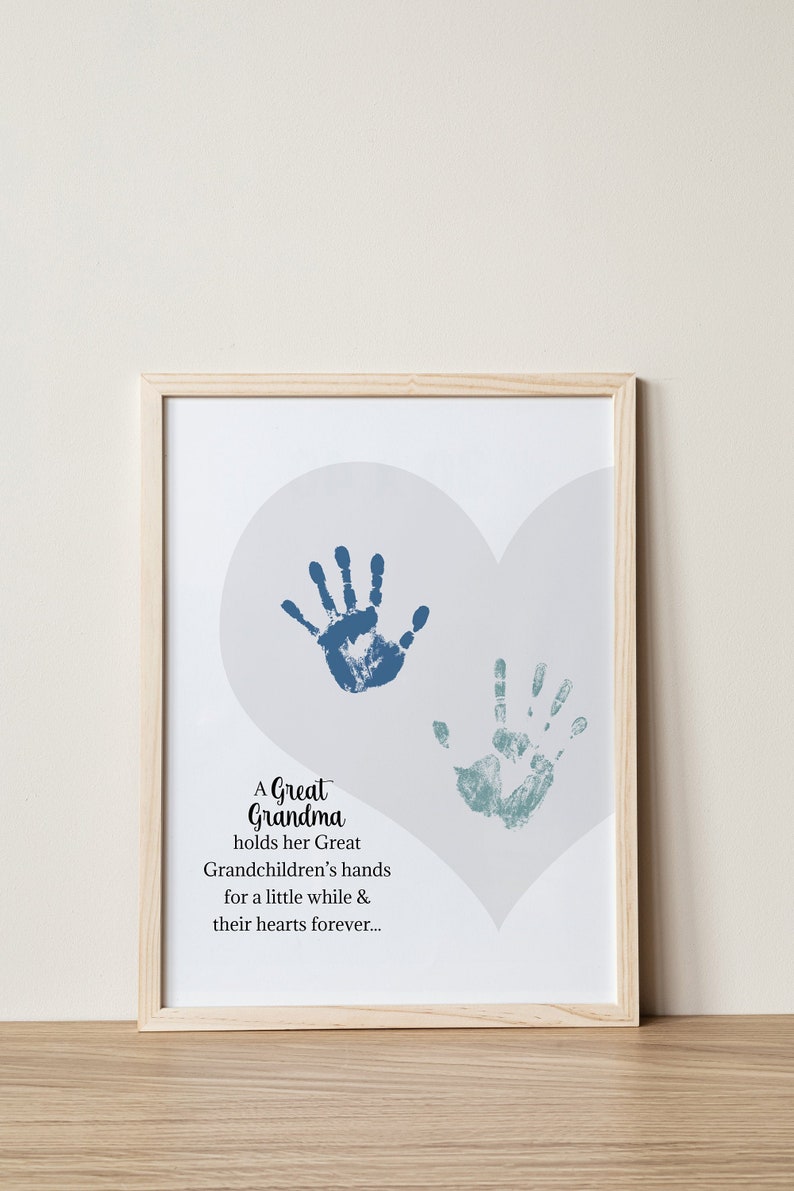 May include: A framed print with a light gray background and two blue handprints in the shape of a heart. The text reads "A Great Grandma holds her Great Grandchildren's hands for a little while & their hearts forever..."
