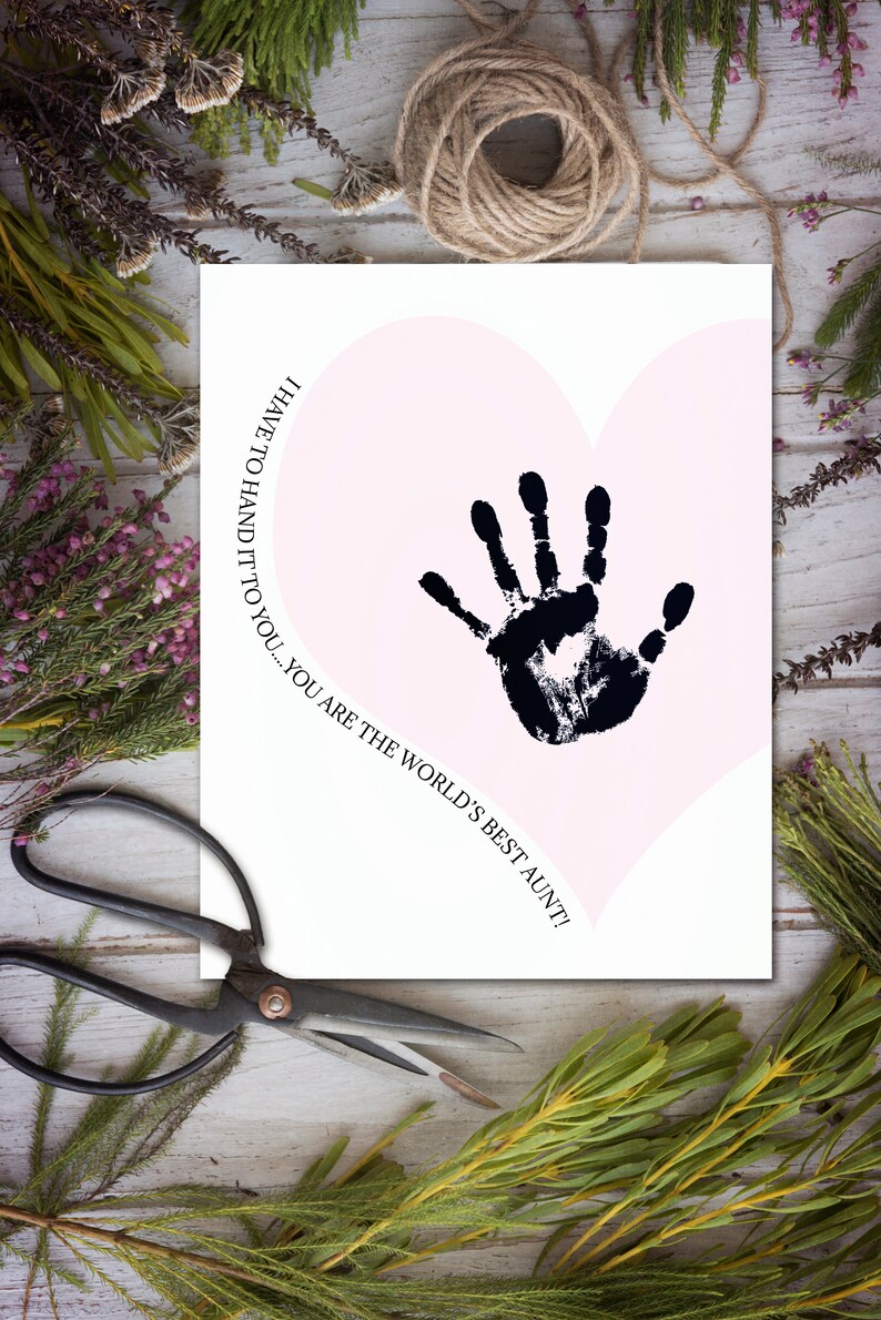 K&ouml;nnte beinhalten: Eine wei&szlig;e Karte mit einer rosa Herzform und einem schwarzen Handabdruck darin. Der Text auf der Karte lautet: "Ich muss es dir sagen... du bist die beste Tante der Welt!"