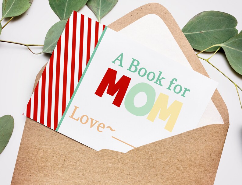 May include: A greeting card with the text "A Book for MOM" in red, green, and yellow, inside a brown envelope. The card has a red and white striped pattern on the left side. Eucalyptus leaves are in the background.