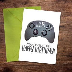 May include: A white card with a black and gray video game controller graphic. The text on the card reads "Level 13 Unlocked" and "You leveled up! Happy Birthday!"