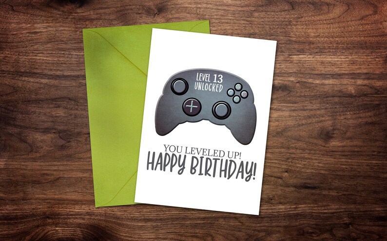 May include: A white card with a black and gray video game controller graphic. The text on the card reads "Level 13 Unlocked" and "You leveled up! Happy Birthday!"