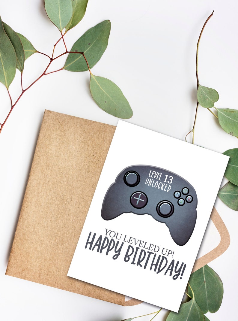 May include: A white card with a black and gray video game controller graphic. The text "Level 13 Unlocked" is above the controller. The text "You Leveled Up! Happy Birthday!" is below the controller.
