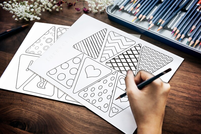 A hand is seen holding a pencil crayon about to start coloring in the pennant flags.