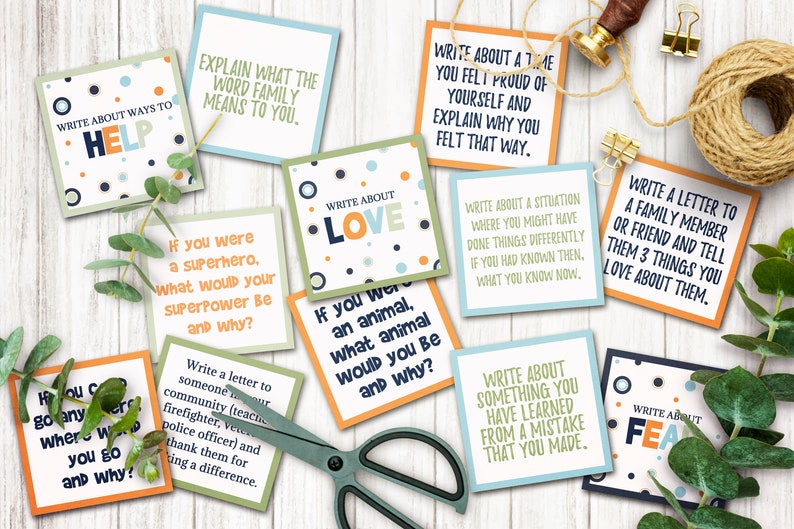 May include: A set of colorful cards with prompts for writing exercises. The cards feature different colors and patterns, including blue, green, orange, and white. The text on the cards includes phrases like "Write about ways to help", "Write about love", and "Write about a time you felt proud of yourself".