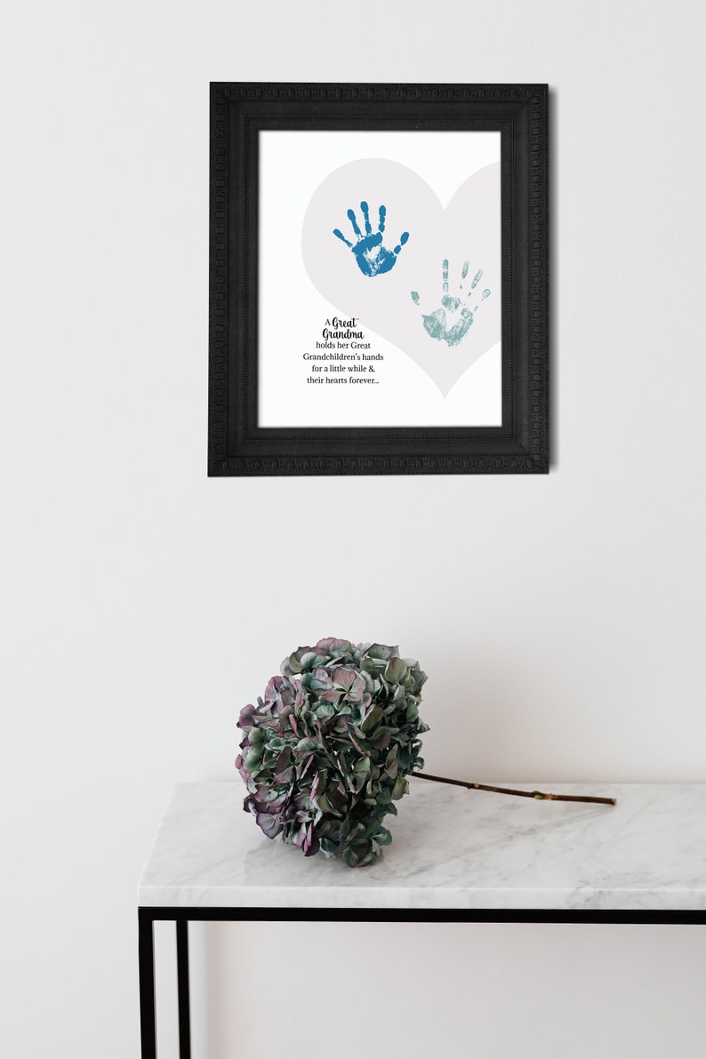 May include: A framed print with a white heart shape and two blue handprints inside. The text reads "A Great Grandma holds her Great Grandchildren's hands for a little while & their hearts forever."
