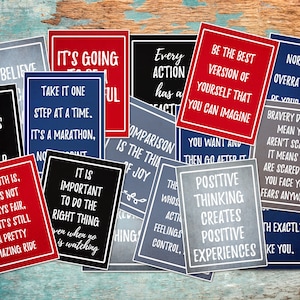 May include: A collection of motivational quote cards with various inspirational messages. The cards are printed on a textured paper with a chalkboard-like appearance. The cards are in red, blue, and gray colors with white text.