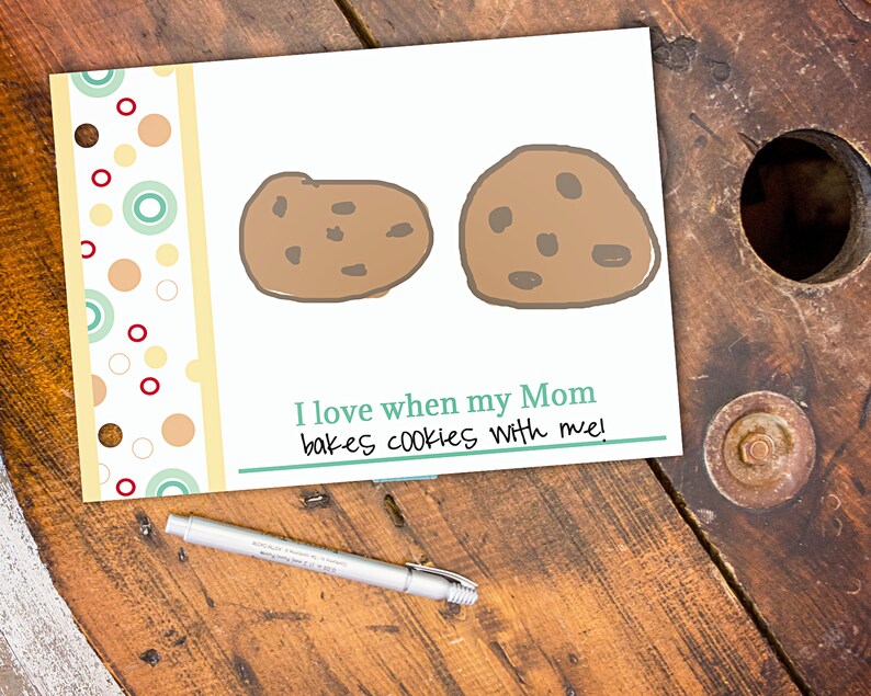 May include: A white card with two cartoon cookies and the text "I love when my Mom bakes cookies with me!". The card has a decorative border with colorful circles and a pen.