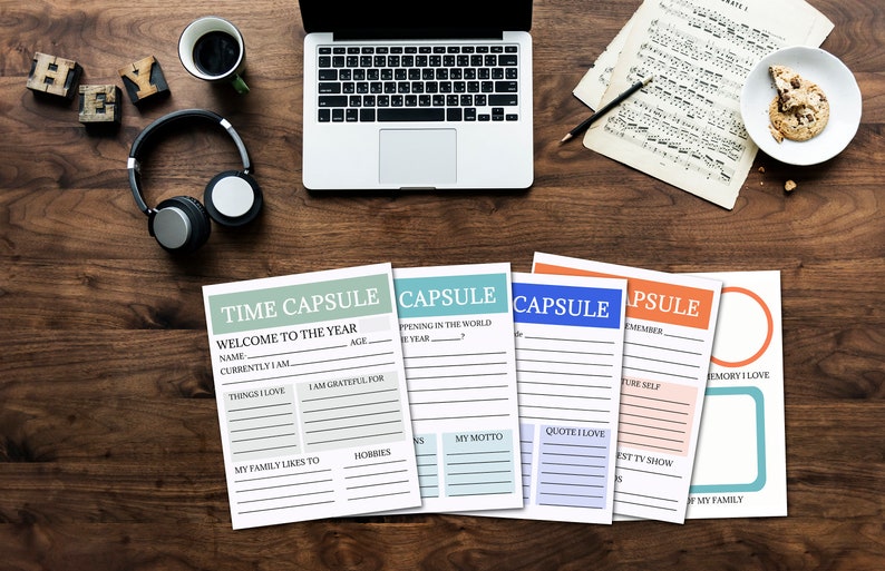 A tabletop is seen with a laptop, a mug of coffee, headphones, sheet music and a plate of cookies. Beneath these items, 5 printed pages sit, the words Time Capsule can be clearly seen, along with spots for writing in details and answers.