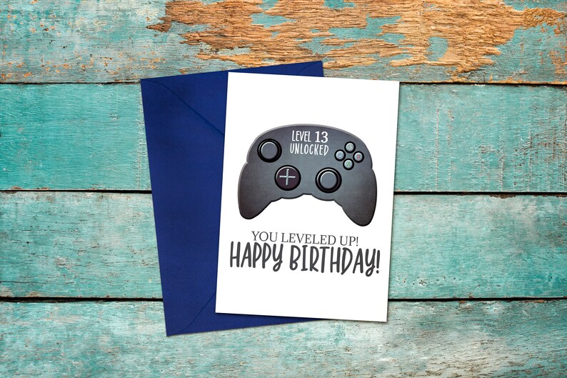 May include: A white card with a black and gray video game controller graphic. The text on the card reads "Level 13 Unlocked" and "You Leveled Up! Happy Birthday!"