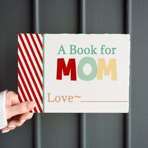 May include: A rectangular book with the text "A Book for MOM" in red, green, and yellow letters. The book has a red and white striped design on the left side and the word "Love" with a line for a signature.