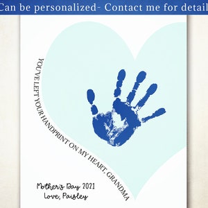 K&ouml;nnte beinhalten: Ein blauer Handabdruck auf einem hellblauen Herzen mit dem Text "YOU'VE LEFT YOUR HANDPRINT ON MY HEART, GRANDMA" und "Mother's Day 2021 Love, Paisley" darunter.