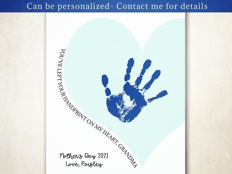 K&ouml;nnte beinhalten: Ein blauer Handabdruck auf einem hellblauen Herzen mit dem Text "YOU'VE LEFT YOUR HANDPRINT ON MY HEART, GRANDMA" und "Mother's Day 2021 Love, Paisley" darunter.