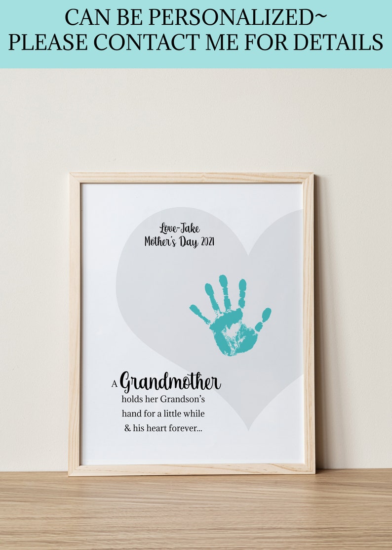 May include: A framed print with a light gray heart shape and a teal handprint inside. The text reads "Love-Jake Mother's Day 2021" and "A Grandmother holds her Grandson's hand for a little while & his heart forever..."