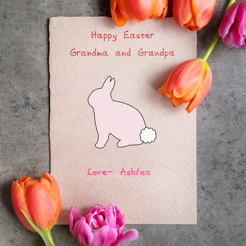 May include: A pink bunny rabbit with a white tail is drawn on a light brown card. The card has the text "Happy Easter Grandma and Grandpa Love - Ashlea" written on it. The card is surrounded by orange and pink tulips.