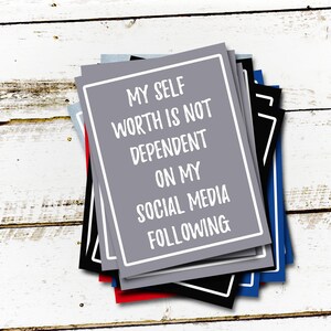 May include: A stack of gray, black, blue, and red cards with white text that reads "My self worth is not dependent on my social media following."