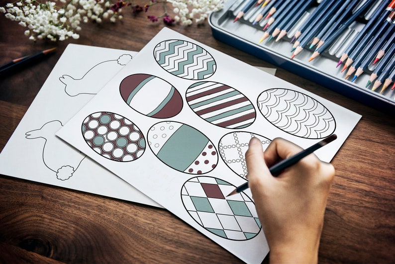 May include: A sheet of paper with eight outlined Easter eggs, each with a different pattern. A person is coloring one of the eggs with a pencil.