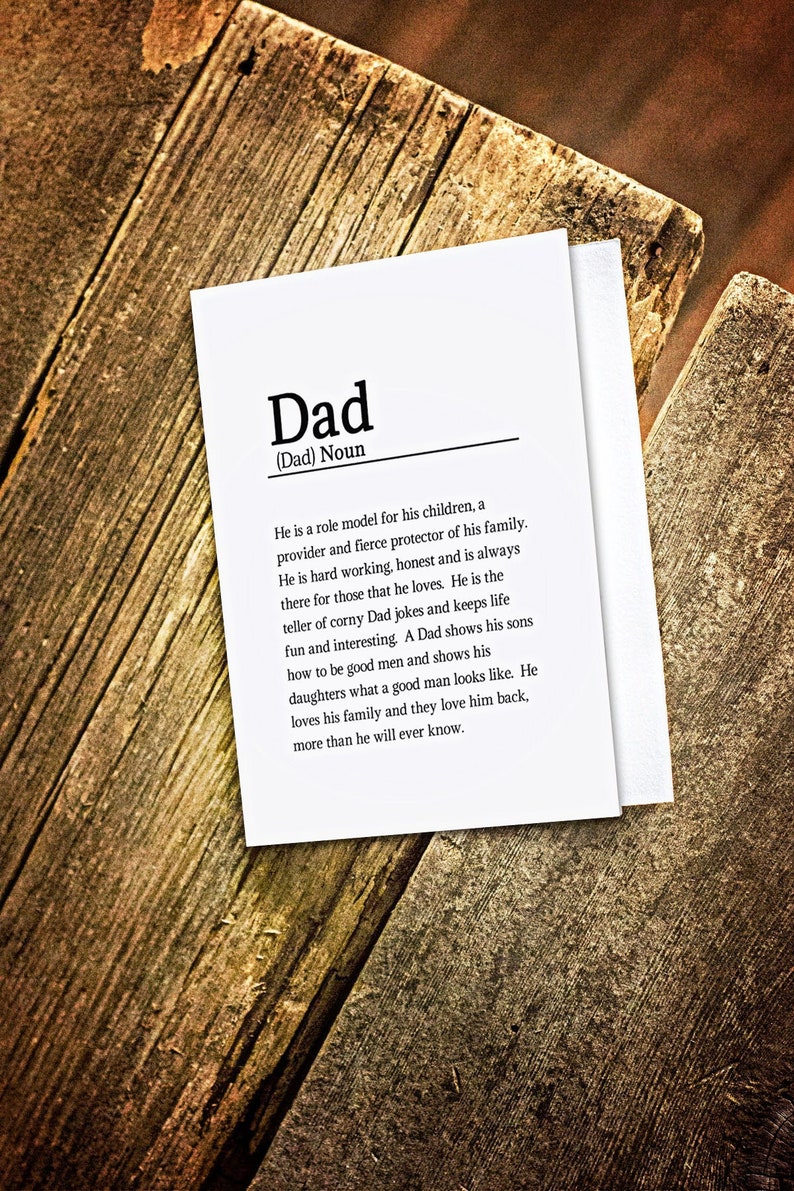 May include: A white card with black text defining the word "Dad" as a role model, protector, and provider for his family. The card is on a wooden surface.