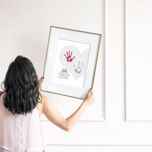May include: A framed print with a white background and a heart shape with two handprints inside. The handprints are red and blue. The text below the handprints reads "A small handprint, a Grandparent's love, a memory to cherish, a gift from above".