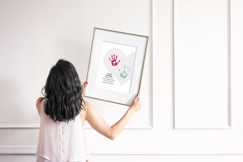 May include: A framed print with a white background and a heart shape with two handprints inside. The handprints are red and blue. The text below the handprints reads "A small handprint, a Grandparent's love, a memory to cherish, a gift from above".
