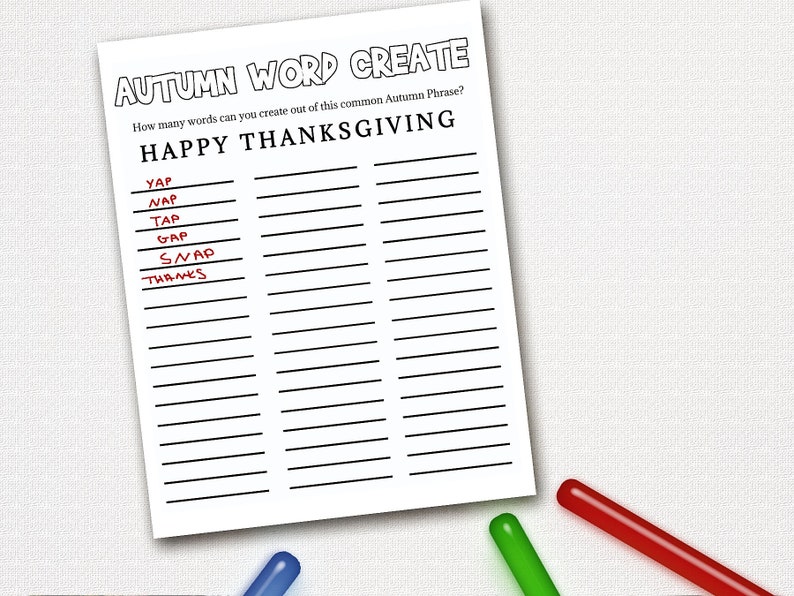 May include: A white paper with the text "AUTUMN WORD CREATE" and "HAPPY THANKSGIVING". Several words are written on the paper, with some highlighted in red. Three colored markers, blue, green, and red, are at the bottom.