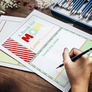 May include: A Book for Mom printable pages with colorful text and decorative borders. The pages include prompts like "My Mom is" and "Thank You, Mom!" A hand is writing with a pencil on one of the pages. Colored pencils are in a metal tin.