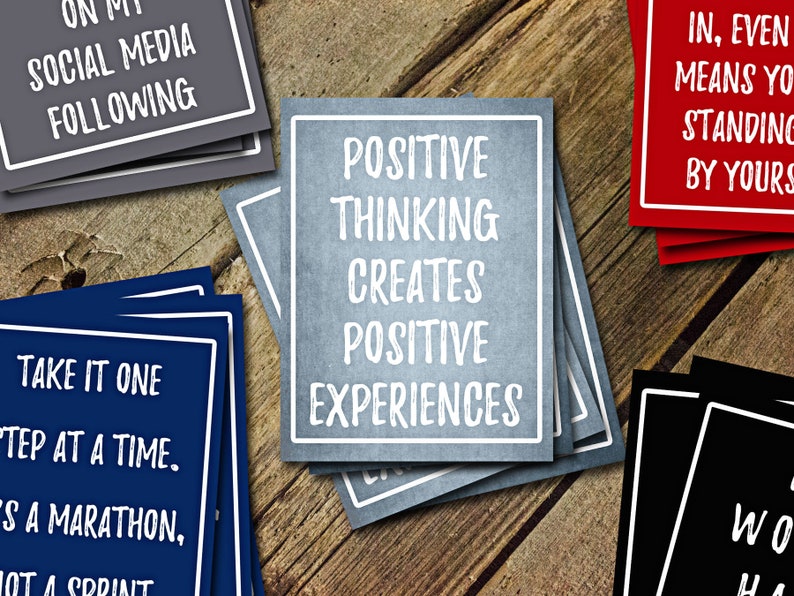 May include: A set of motivational cards with positive messages. The cards are blue, red, black, and gray with white text. The text on the blue card reads "Take it one step at a time. It's a marathon, not a sprint". The text on the red card reads "In, even means you're standing by yours". The text on the gray card reads "Positive thinking creates positive experiences".