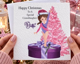 May include: A square greeting card featuring a cartoon gymnast in a purple leotard and Santa hat standing on a purple gift box. Next to the gymnast is a pink Christmas tree. The text reads Happy Christmas To A Special Granddaughter Dottie.