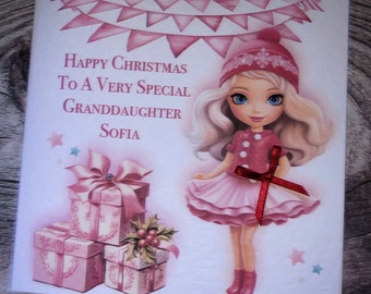 Può includere: Un biglietto di Natale rosa con una bambina dei cartoni animati che indossa un vestito rosa e un cappello rosso. Il biglietto dice "Buon Natale a una nipote molto speciale Sofia".