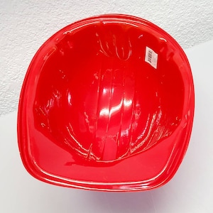 May include: Red plastic construction worker helmet. The helmet has a smooth, shiny surface and is designed for play.