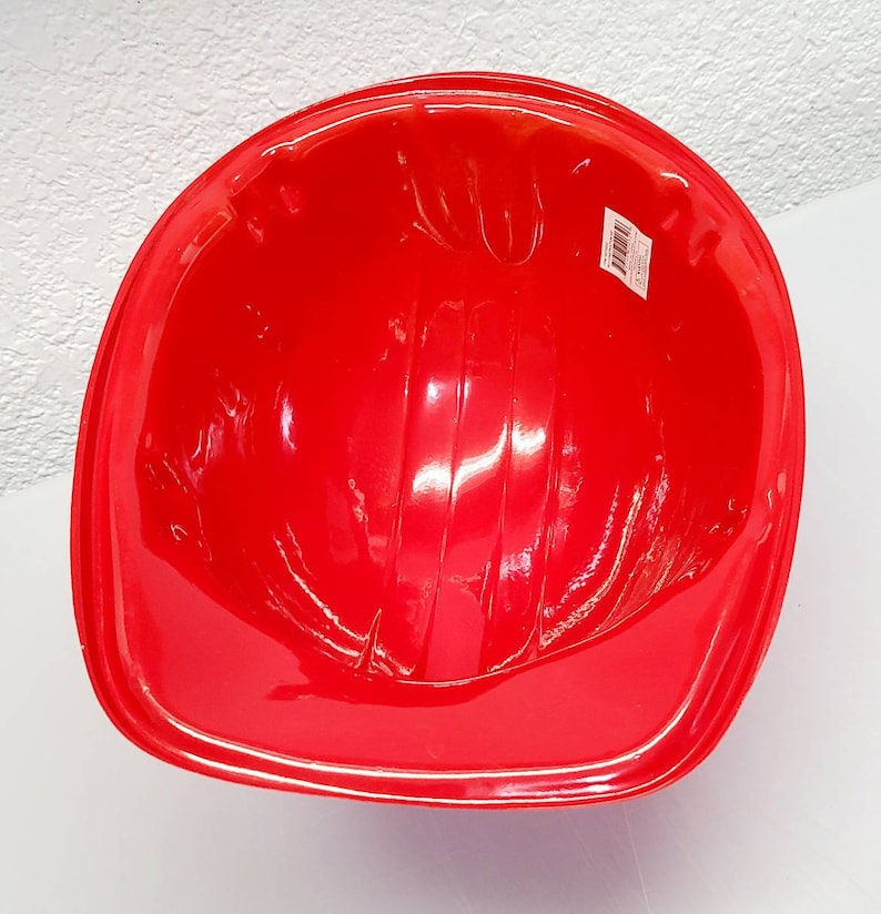 May include: Red plastic construction worker helmet. The helmet has a smooth, shiny surface and is designed for play.