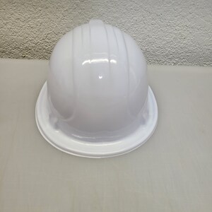May include: A white hard hat with a smooth, glossy finish. The hat has a wide brim and a rounded top.
