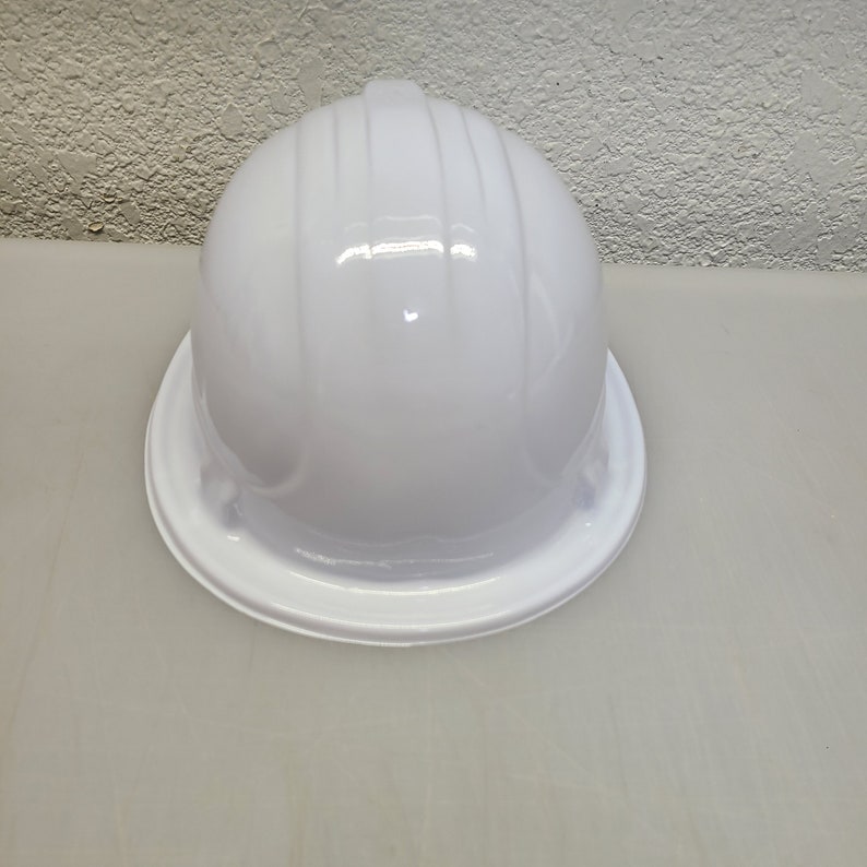May include: A white hard hat with a smooth, glossy finish. The hat has a wide brim and a rounded top.