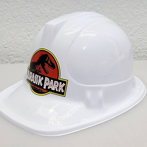 May include: White plastic construction worker hat with a red and black Jurassic Park logo featuring a dinosaur silhouette.