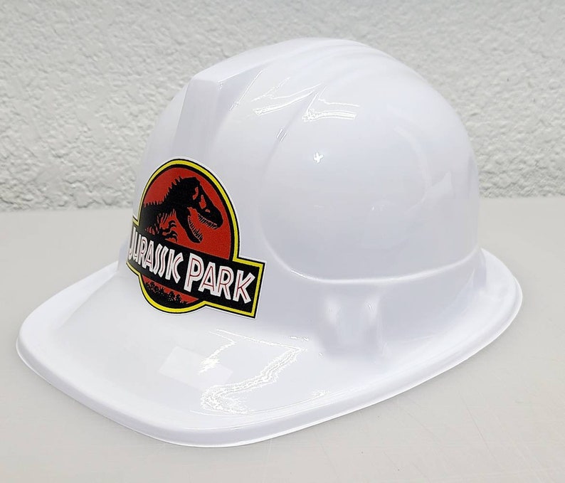 May include: White plastic construction worker hat with a red and black Jurassic Park logo featuring a dinosaur silhouette.