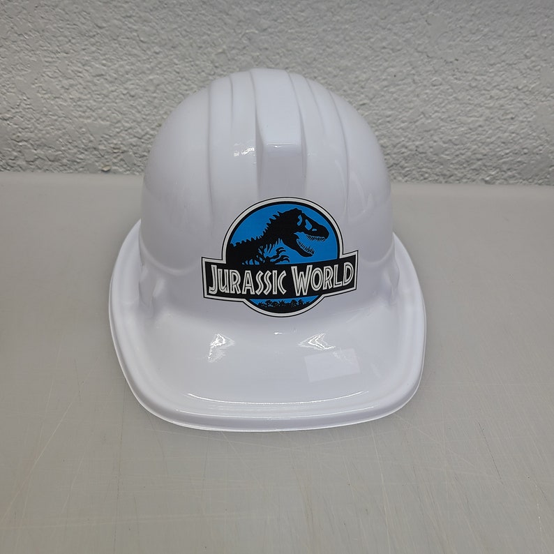 May include: White plastic construction worker hat with a blue and black Jurassic World logo featuring a dinosaur silhouette.