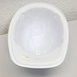 May include: White hard hat with a smooth, glossy finish. The inside of the hard hat is visible, showing the suspension system. The hard hat has a label that reads "WARNING".