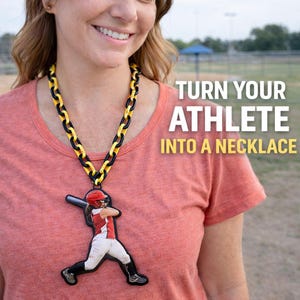 May include: A necklace with a black and yellow chain and a pendant featuring a softball player in a red and white uniform. The text "TURN YOUR ATHLETE INTO A NECKLACE" is displayed in white.