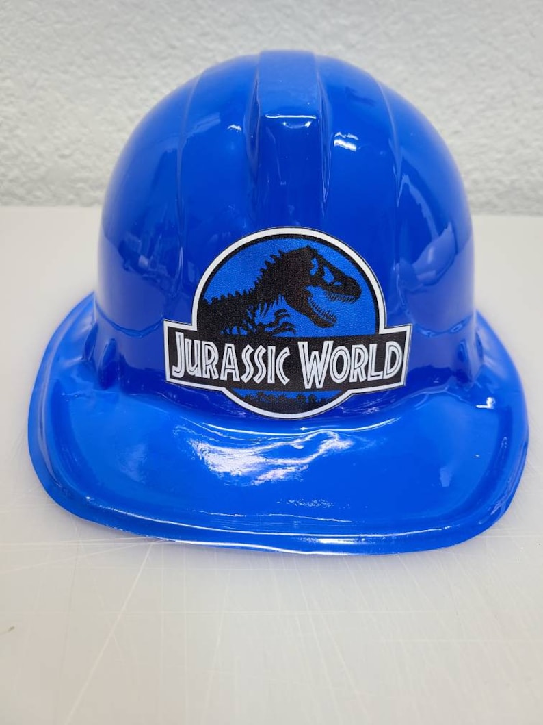 May include: A blue plastic construction worker hat with a Jurassic World logo featuring a dinosaur silhouette.