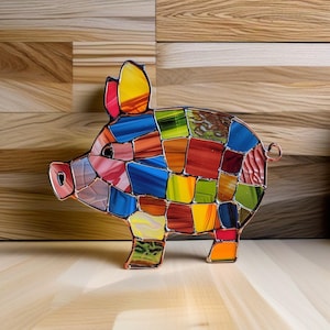 Puede incluir: Una figurita de cerdo de vidrio coloreado con un diseño de mosaico en tonos de rojo, azul, verde, amarillo y naranja. El cerdo está hecho de vidrio y tiene un marco de alambre.