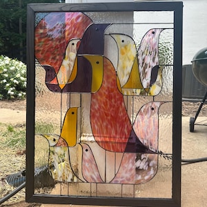 Könnte beinhalten: Ein rechteckiges Buntglasfenster in einem dunklen Holzrahmen mit einer abstrakten Komposition aus mehreren Vogelformen. Die Vögel bestehen aus strukturierten und mehrfarbigen Glasstücken in den Farben Rot, Gelb, Violett und Weiß.