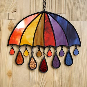 May include: A stained glass rainbow umbrella with raindrops hanging from the bottom. The umbrella is made of red, orange, yellow, green, blue, indigo, and violet glass.