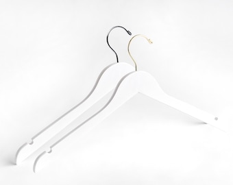 May include: Two white wooden hangers with black and gold metal hooks. The hangers are stacked on top of each other.