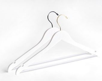 May include: Two white wooden hangers with black and gold hooks. The hangers are stacked on top of each other.